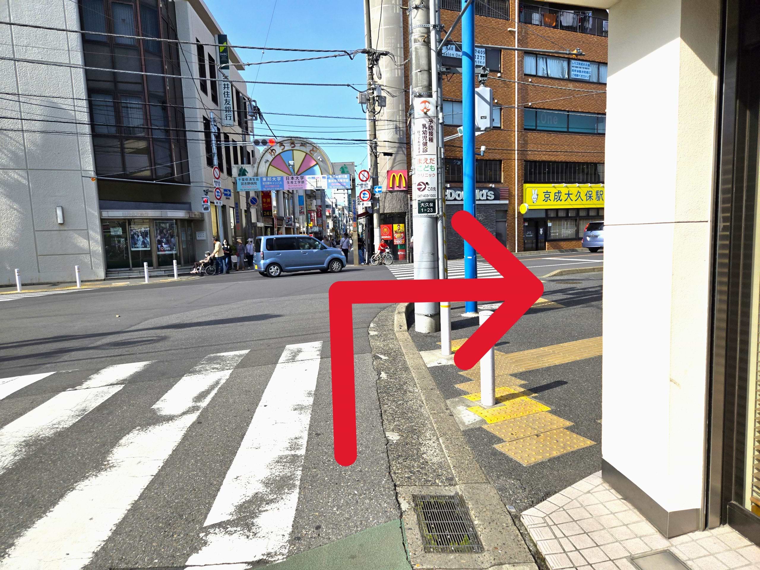 ミスタードーナツ 京成大久保駅前ショップを右手に直進し、大久保商店街 ゆうロード入口前交差点まで進んだら横断歩道を渡らずに右折します
