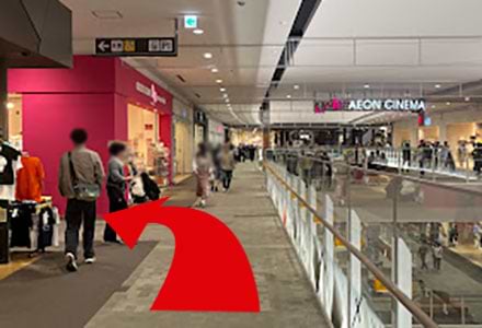 エスカレーターを降りたら、イオンシネマ方面へ直進し、「Dream market」さん（ピンクの店舗）を目印に左へお曲がりください。<br />