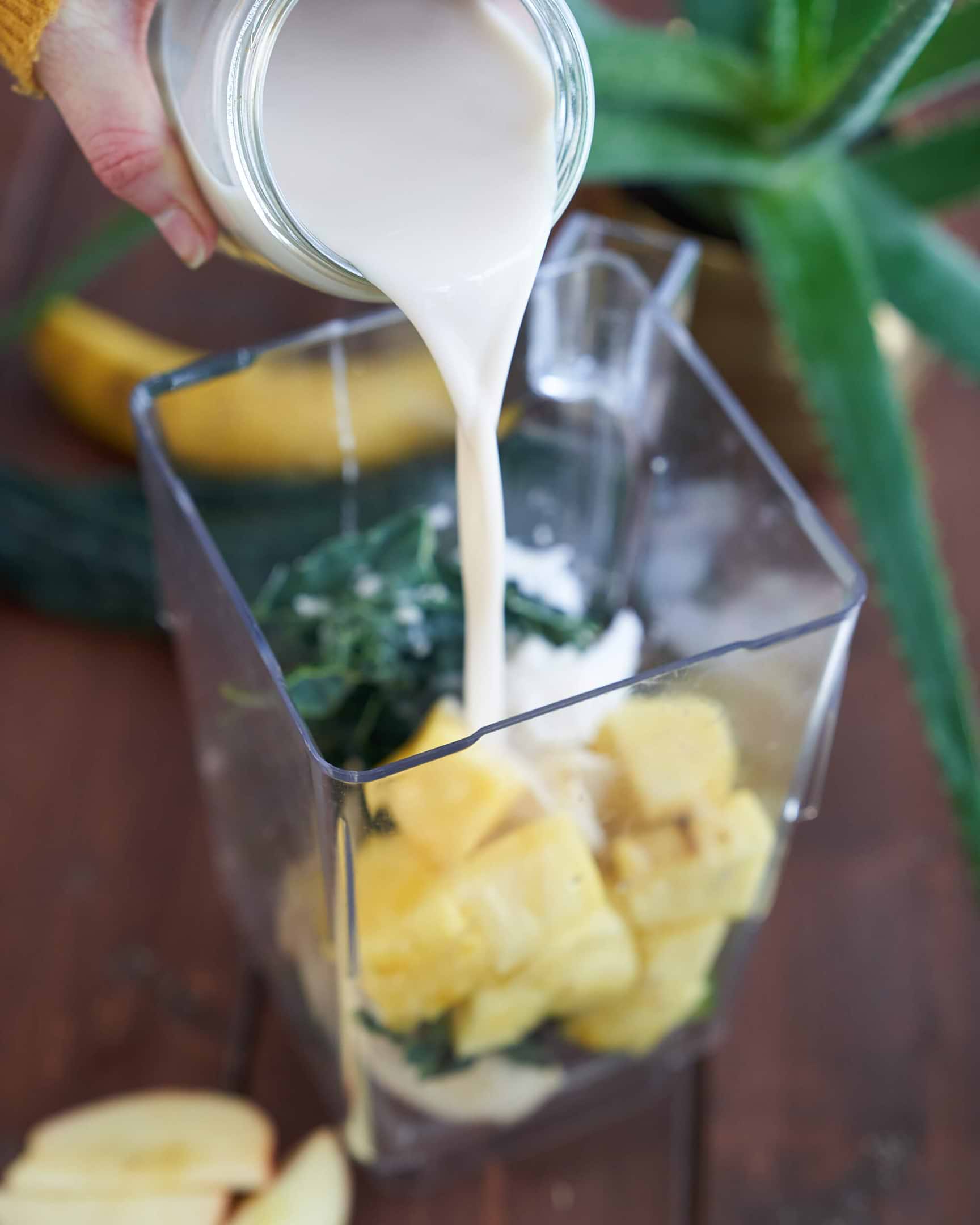 Pouring Oat Milk Into Green Aloe Smoothie with Kale, Pineapple and Banana