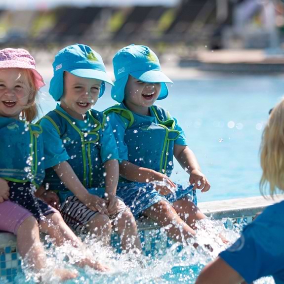 Three young children splashing in pool with nanny