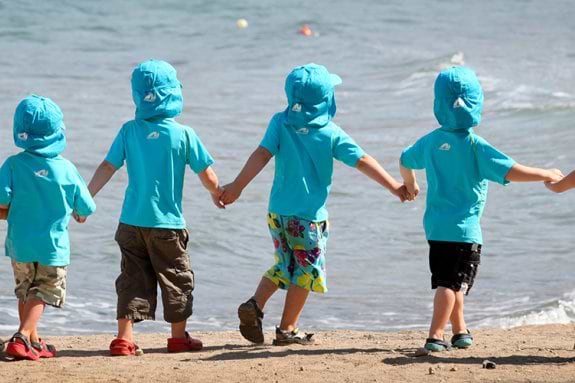 group of toddlers holdimg hands and walking along the beach