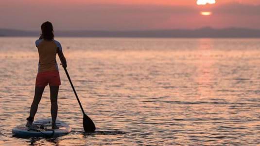Two women stand up paddle boarding at sunset