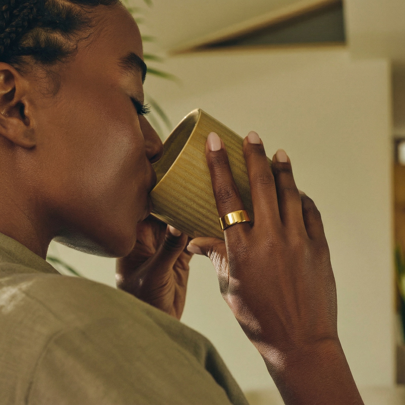 Ultrahuman Ring AIR in gold, on a hand holding a cup