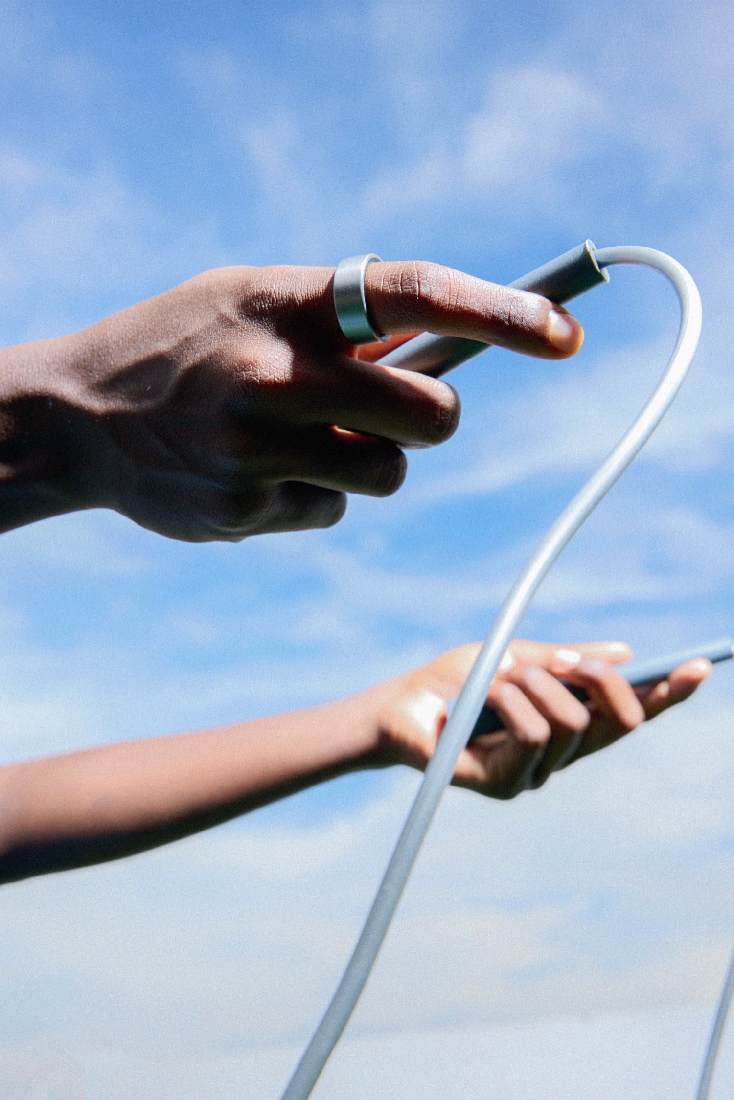 Ultrahuman Ring AIR on a hand reaching for a cable against the sky