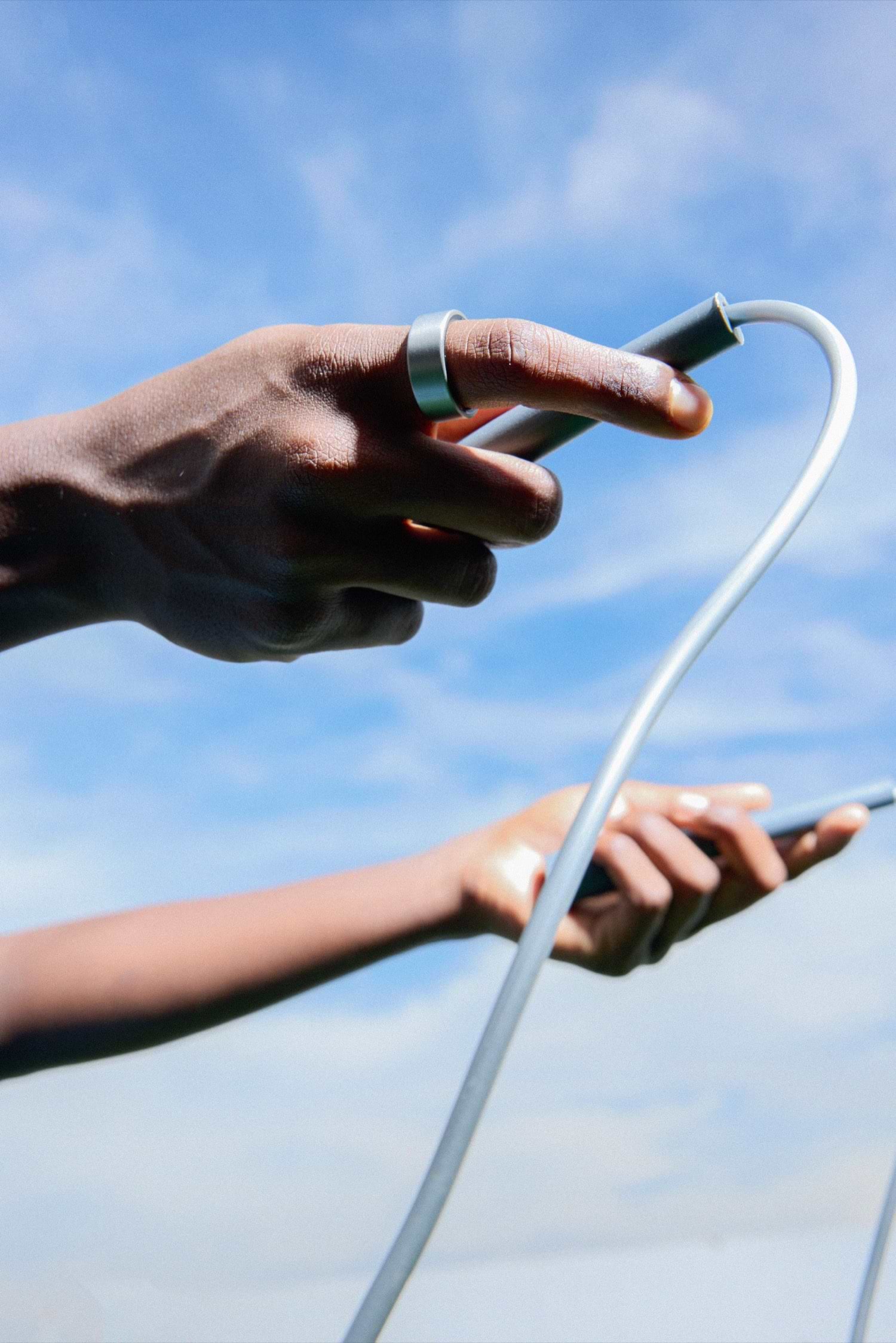 Ultrahuman Ring AIR on a hand reaching for a cable against the sky