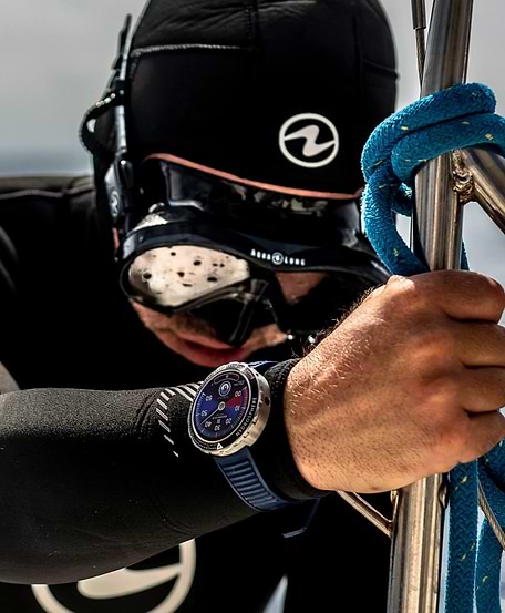 Un plongeur en tenue noire ajuste une corde sur une structure métallique. Il porte une smartwatch bleuebracelet .