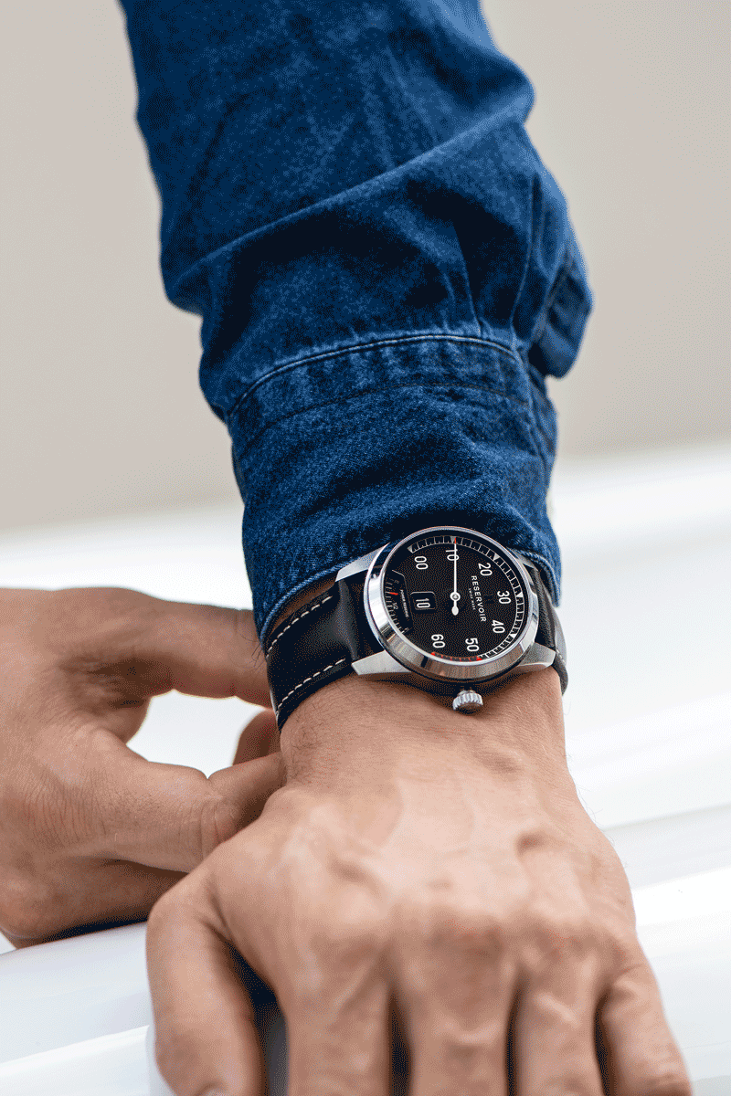Personne en denim ajustant une montre-bracelet à cadran noir avec chiffres blancs et cuir noir bracelet.