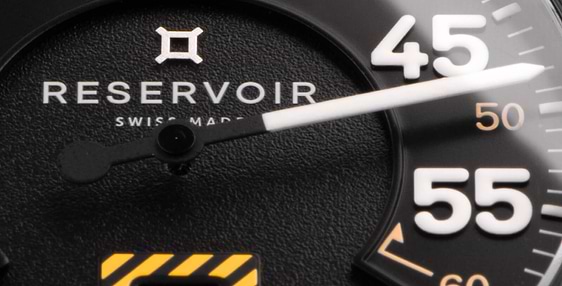 Gros plan du cadran d'une montre-bracelet Reservoir affichant des chiffres blancs, la date et un indicateur de type jauge à carburant.