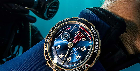 Plongeur sous l&#039;eau, portant un masque noir et une montre &quot;Hydrosphere&quot; avec cadran bleu et bracelet.