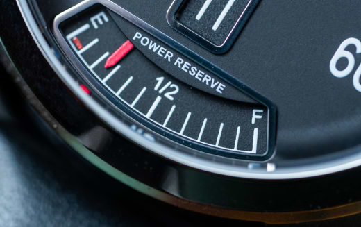 Analog power reserve indicator with red pointer between empty (E) and midpoint (1/2).