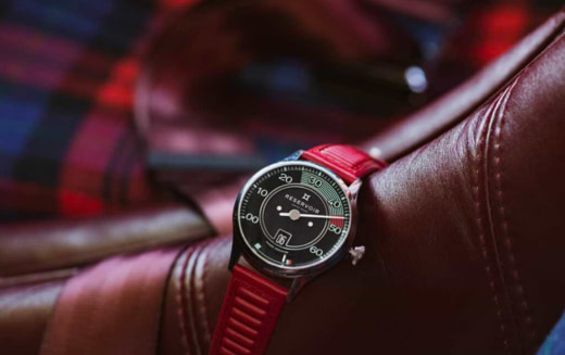 Wristwatch with black dial, red strap, white markers, and Arabic numerals on a leather surface.