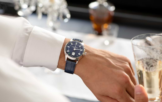 Person in a white shirt wearing a blue wristwatch holds a glass with a light-colored drink.