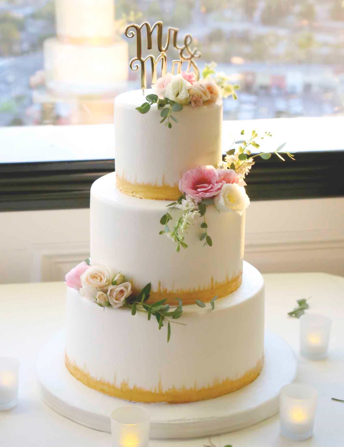 Lillian and Josh's three-tier wedding cake featured gold accents and pink roses