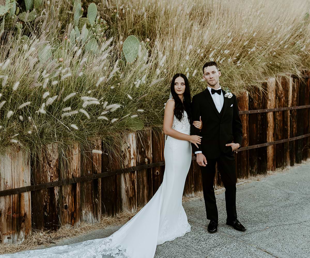 Bride and Groom posing in front of a wooden fence and tall grass at Dove Canyon