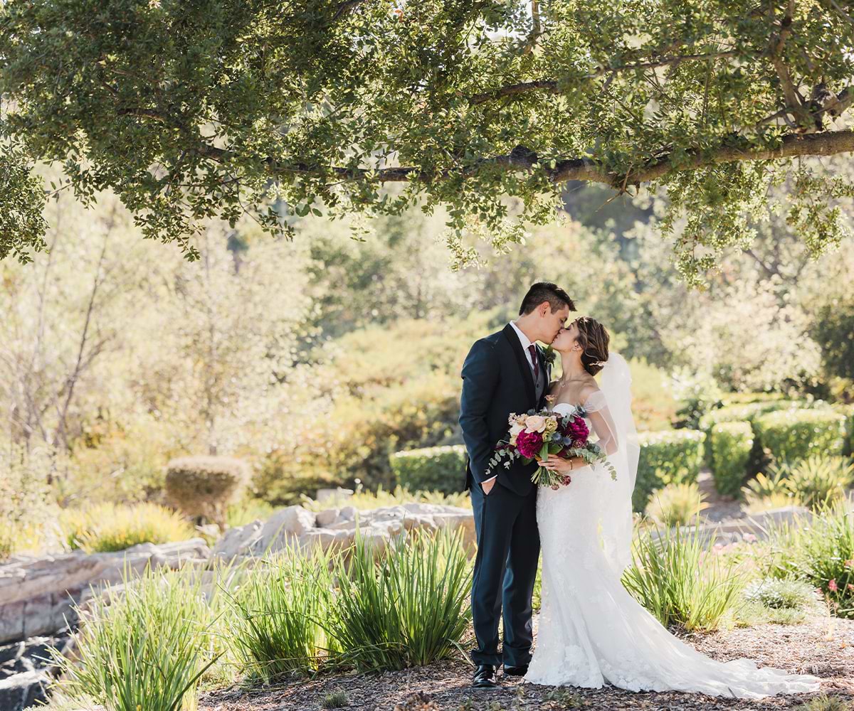 Just married at Dove Canyon by Wedgewood Wedding couple kissing unde a large tree.