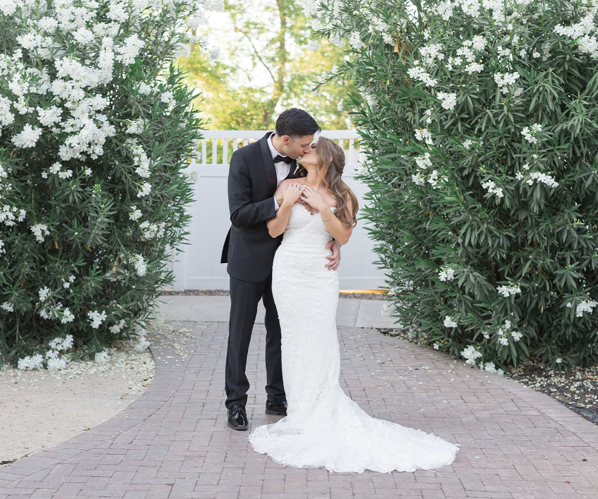 Newlyweds kissing in front of flowers at Lindsay Grove by Wedgewood Weddings