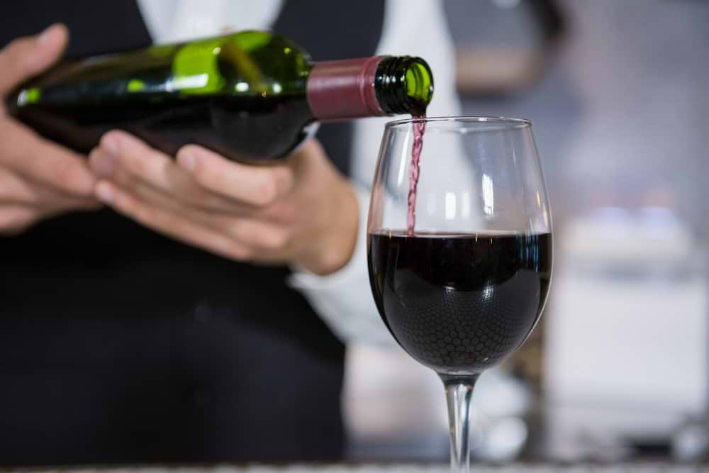 Mid section of bartender pouring red wine on glass in bar counter-1