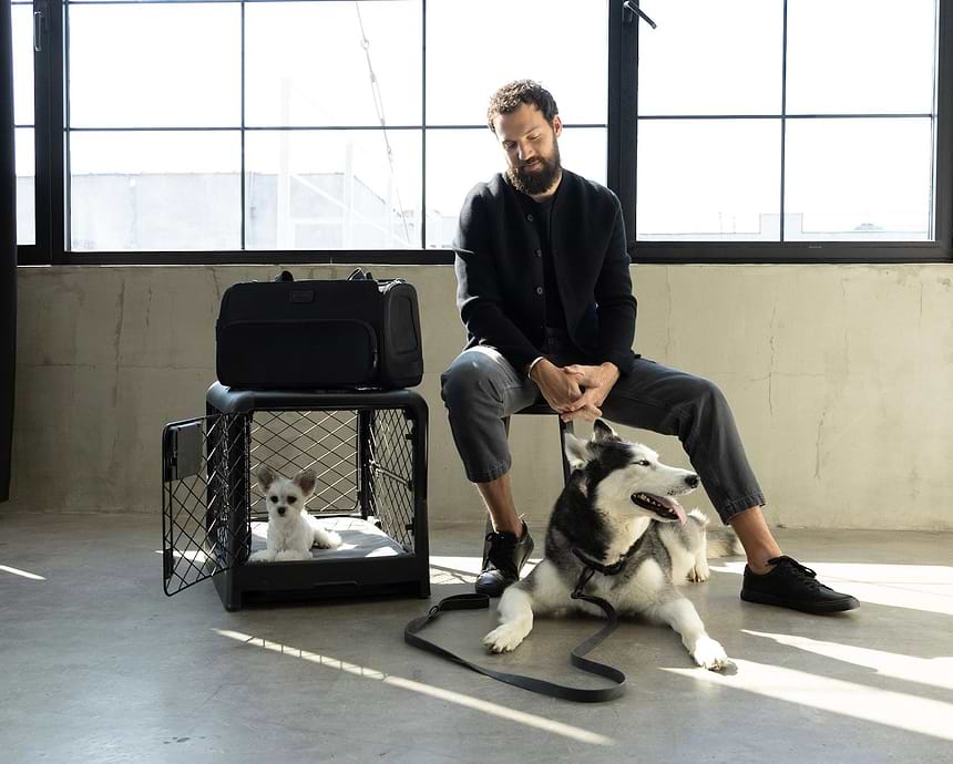 A man sitting with a dog next to a dog crate and carrier
