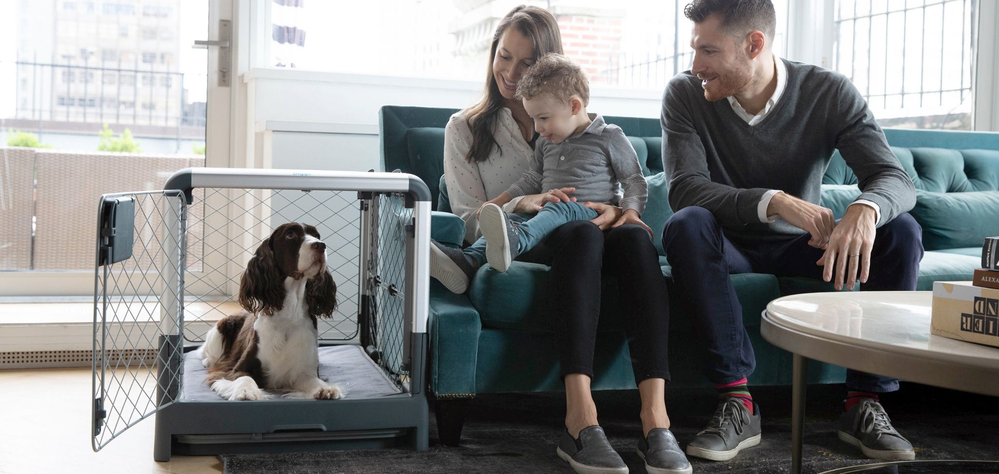  a family sitting on a couch next to their dog in a Grey Revol crate 