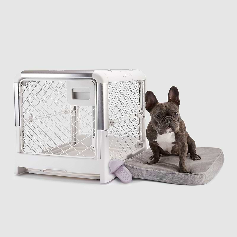 A dog sitting on a Snooz pad next to a Revol dog crate