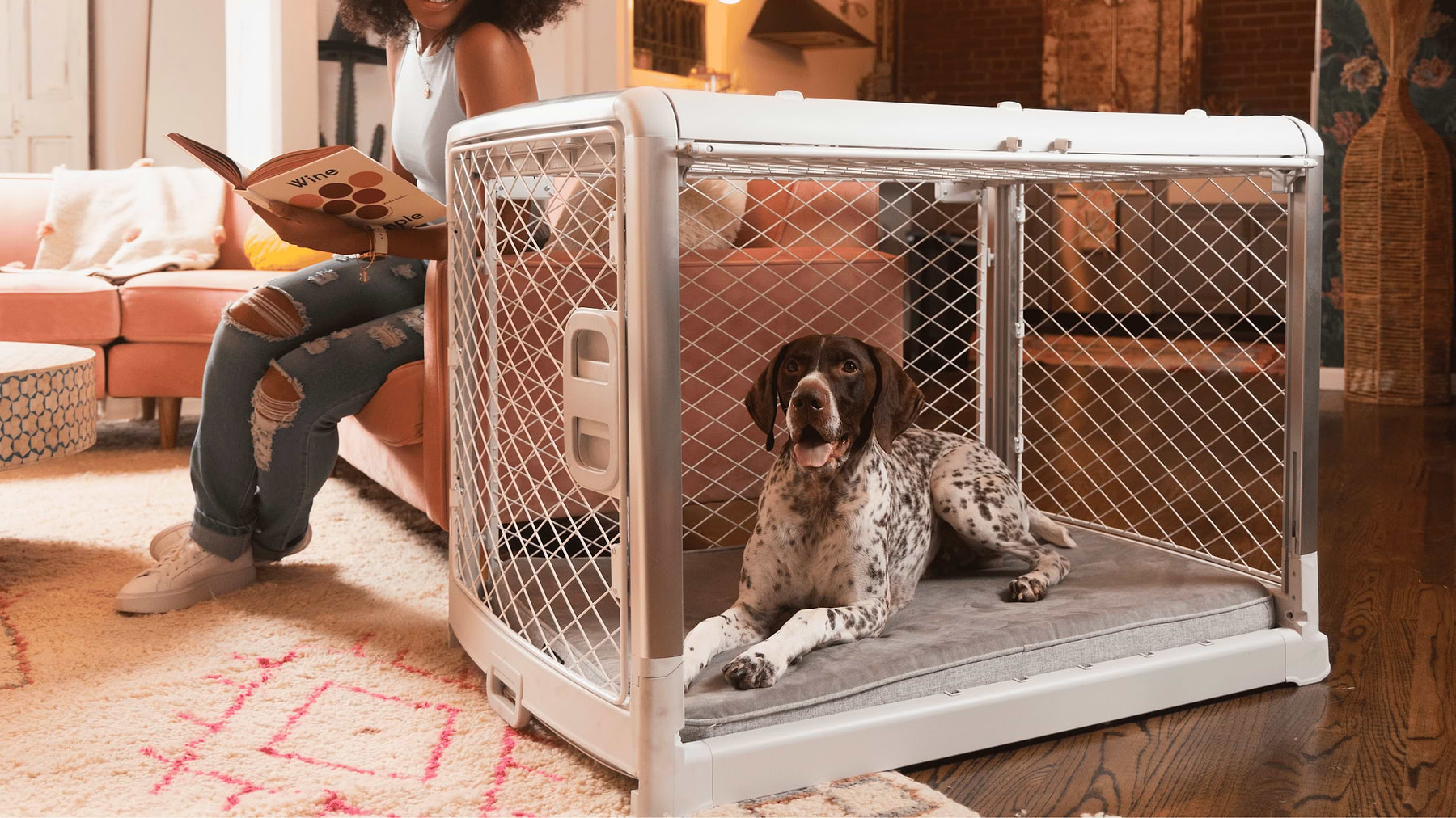  a woman sitting on a couch next to a dog in a Revol crate with the side door open 