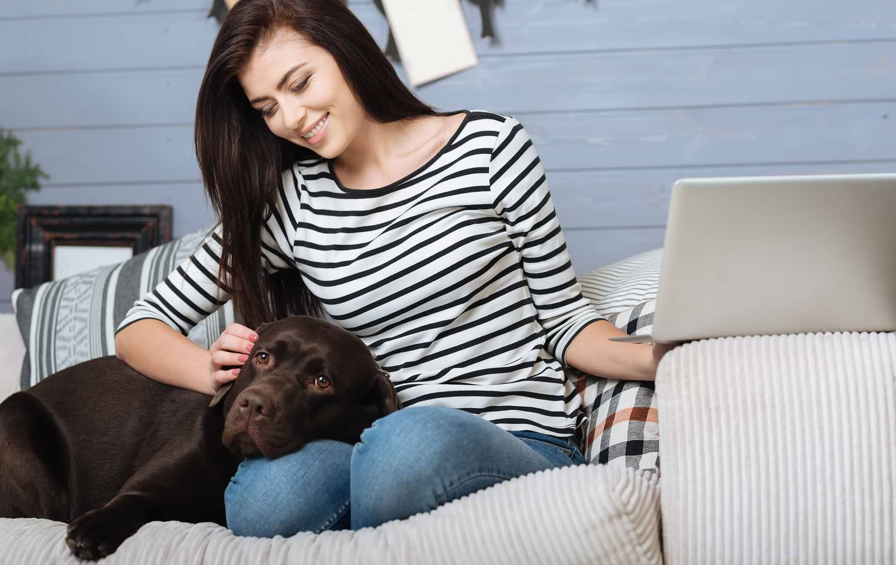  A dark brown dog lying on a girl's lap while they are on the sofa. 