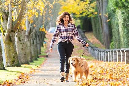 a woman walking a dog down a leaf covered path