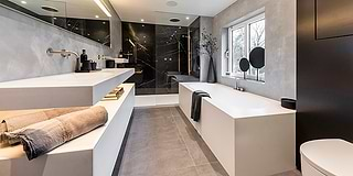 B Dutch produceert in de eigen fabriek in Cuijk badkamer elementen en keukens van onder meer solid surface Corian. Een topkwaliteit materiaal dat nooit verkleurd. De foto toont een badkamer waar maatwerk Corian producten zijn gebruikt, mat wit. In de regendouche zijn de keramische slabs van B Dutch verwerkt. Ook de douchevloer is van B Dutch, evenals alle kranen. Een prachtig voorbeeld van een mooi badkamerontwerp.