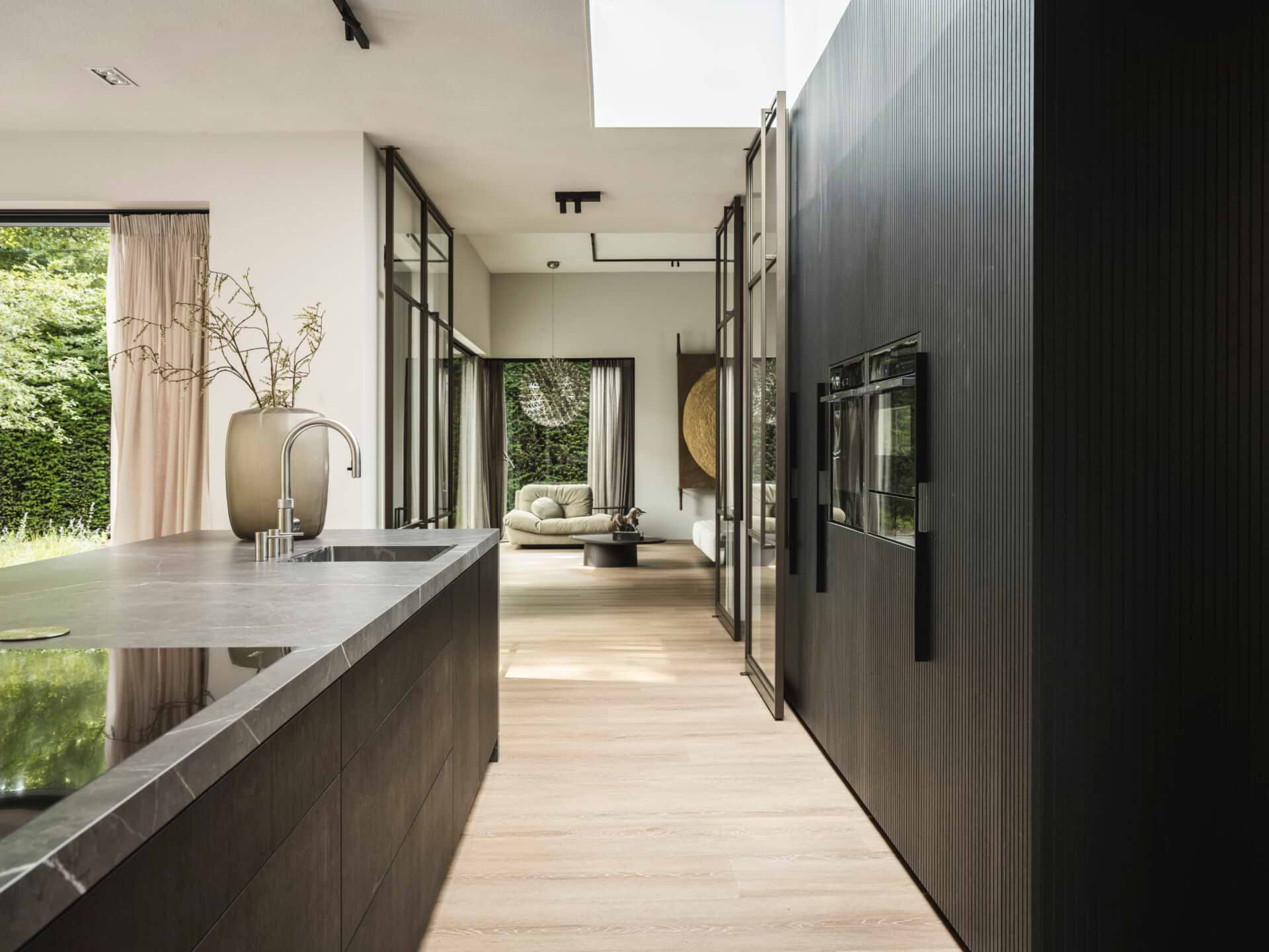 Luxe keuken met keramisch kookeiland grijs marmer look en een apparatenwand van zwart houtfineer. Maatwerk productie B Dutch.