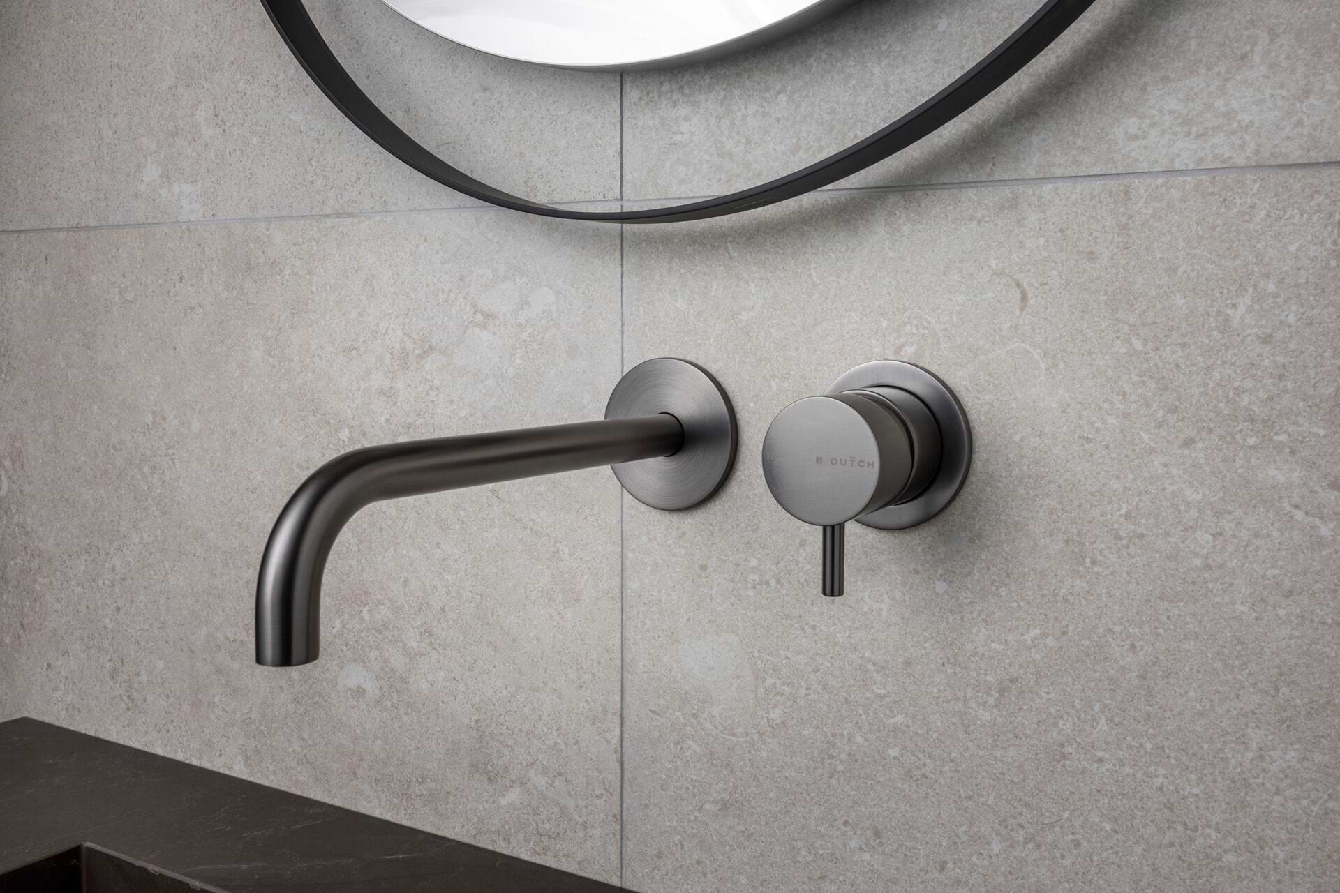Minimalistische wandkraan in Gun Metal met menghendel van B Dutch, gemonteerd op een lichte natuursteen wand.