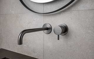 Minimalistische wandkraan in Gun Metal met menghendel van B Dutch, gemonteerd op een lichte natuursteen wand.