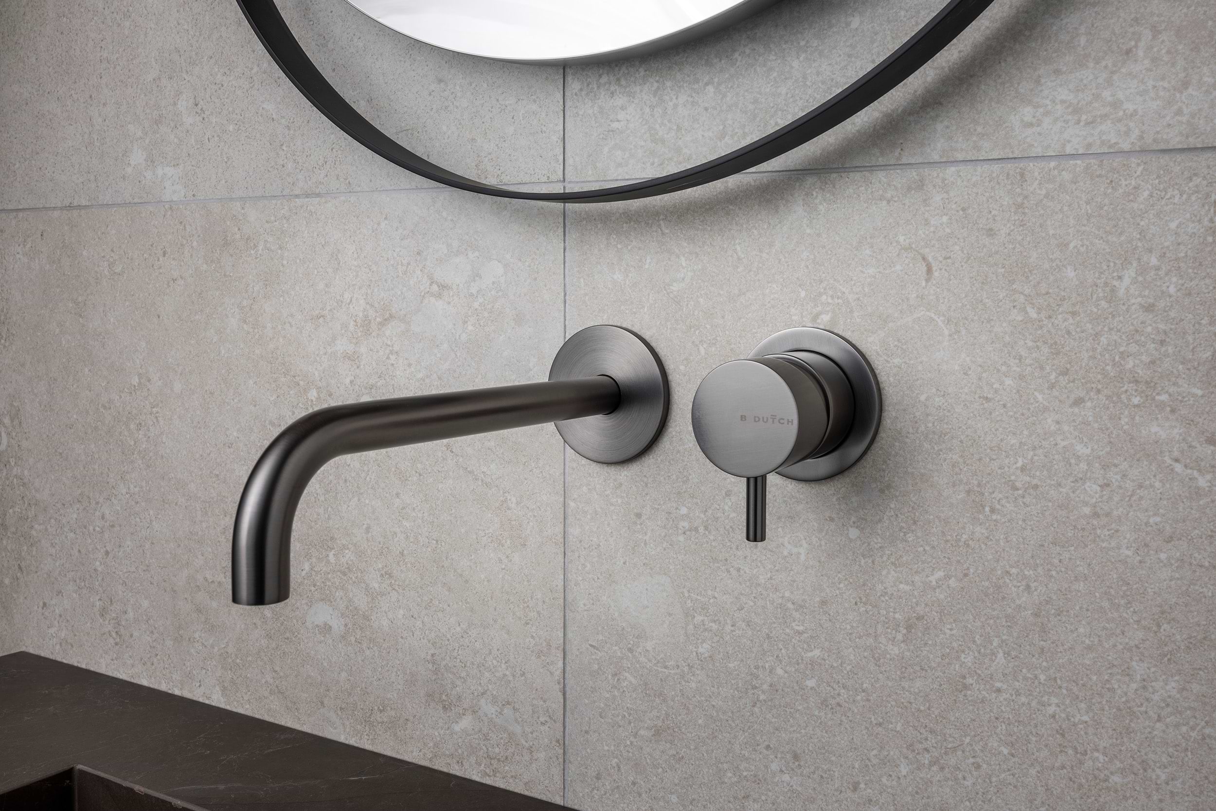 Minimalistische wandkraan in Gun Metal met menghendel van B Dutch, gemonteerd op een lichte natuursteen wand.