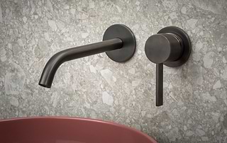 Wandkraan en mengkraan in Gun Metal van B Dutch bij een roze waskom op terrazzo wand, modern en verfijnd.