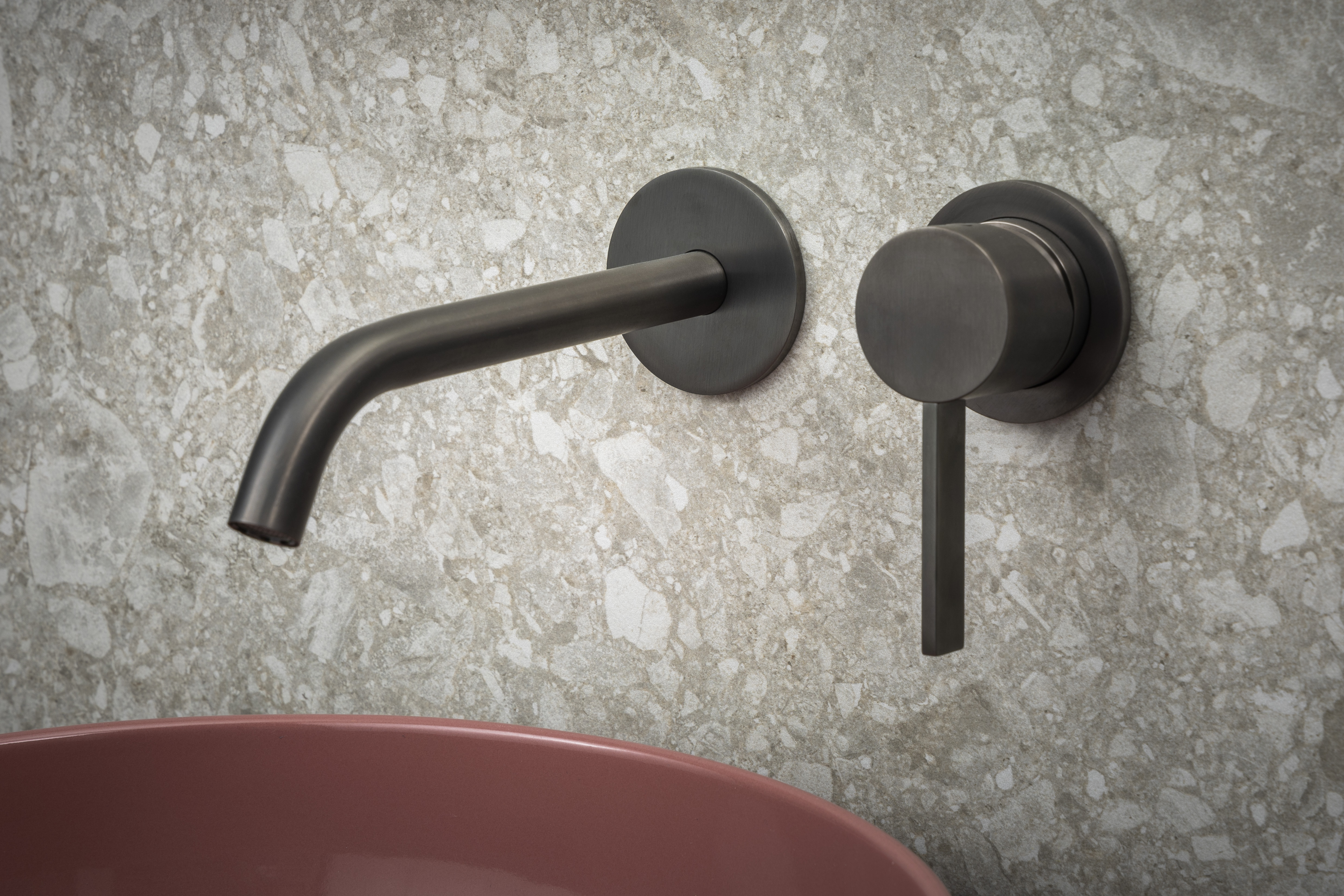 Wandkraan en mengkraan in Gun Metal van B Dutch bij een roze waskom op terrazzo wand, modern en verfijnd.