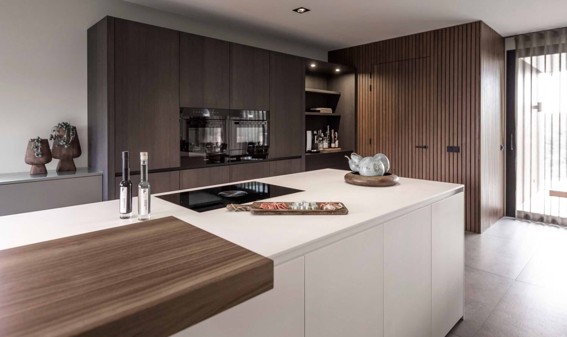 Modern kookeiland in mat wit Solid Surface Corian met warm houtaccent en donker houten kastenwand.