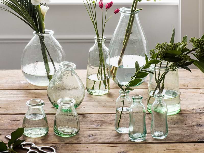 Recycled glass vases on tabletop with assorted stems