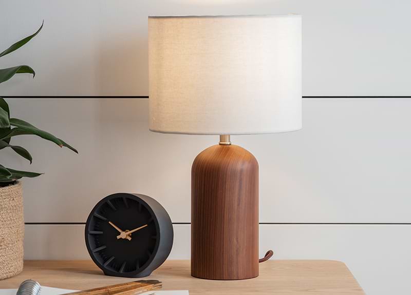A kingsbury walnut table lamp next to a black clock.