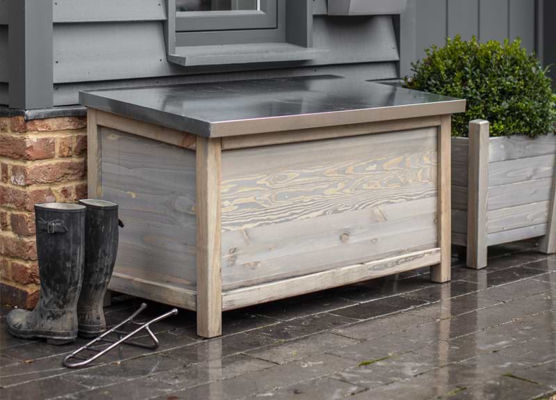 An Aldsworth Outdoor Storage Box with wellington boots, a Farringdon Boot Jack and an outdoor plant.