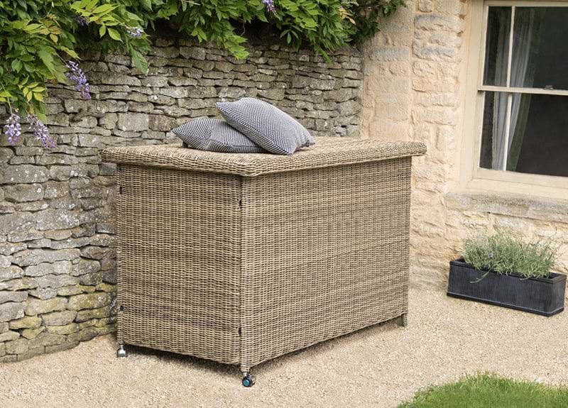 A Marden Cushion Storage Box against a stone garden wall with an outdoor plant box next to it.