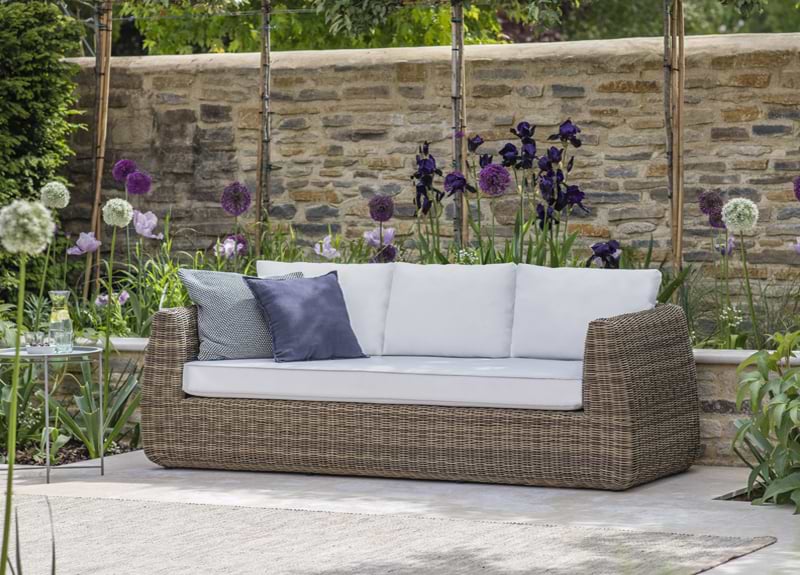 A Scala 3 Seater Sofa in a beautiful garden surrounded by white and purple flowers.