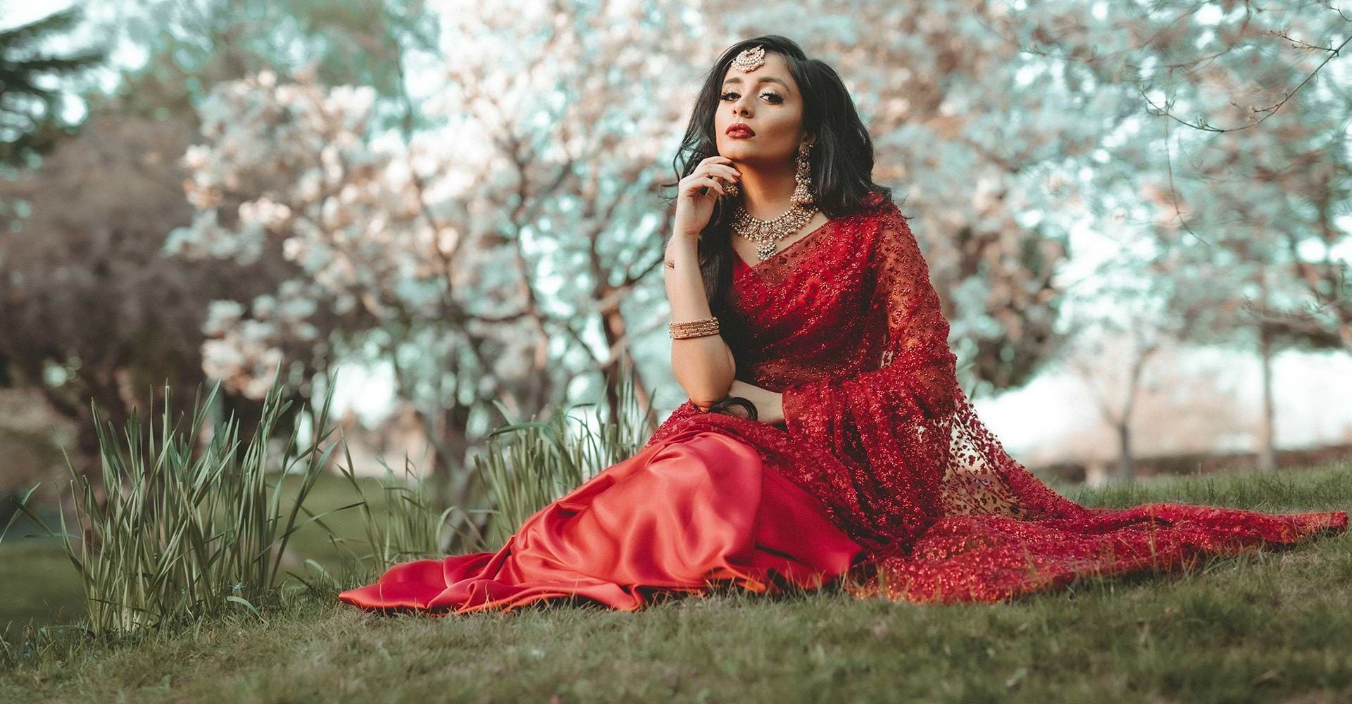A bride sitting on grass in a red South Asian wedding dress