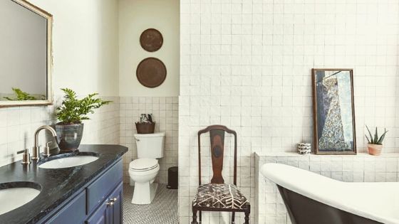 A bathroom environment with square white tiles on the walls and a black an white pattern tile on the floor