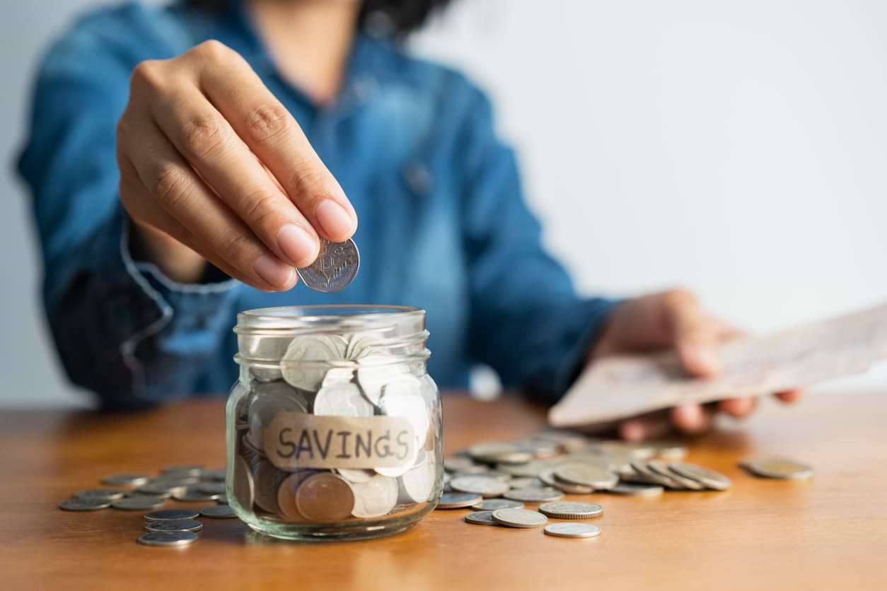 A lady putting quarters into a small glass savings jar 