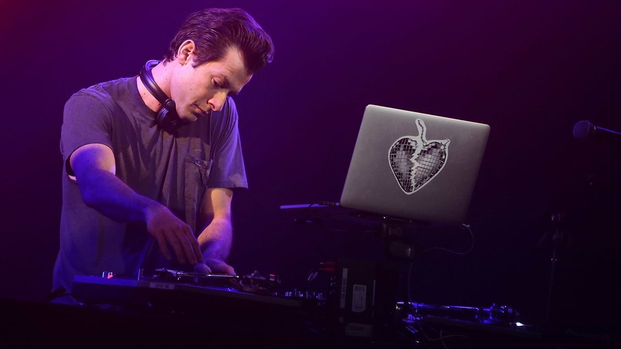 Mark Ronson standing behind his computer while playing music at a concert