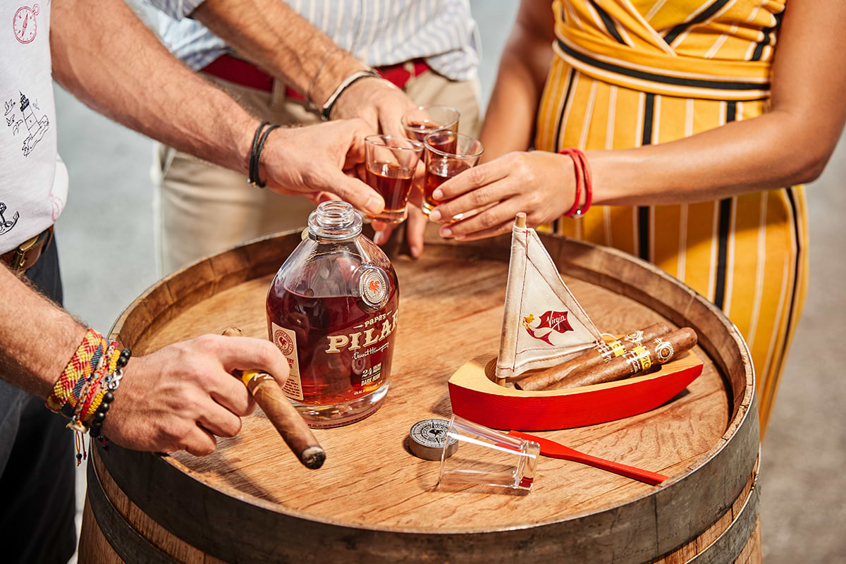Two man and a woman around a barrel table while holding glasses of rum