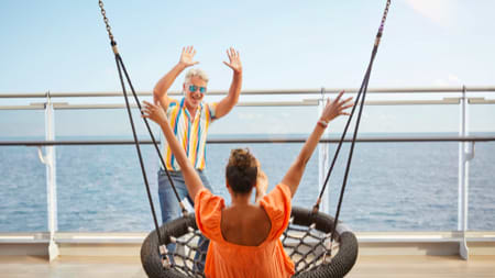 Woman in swing man cheering the woman on with ocean ship deck view in background