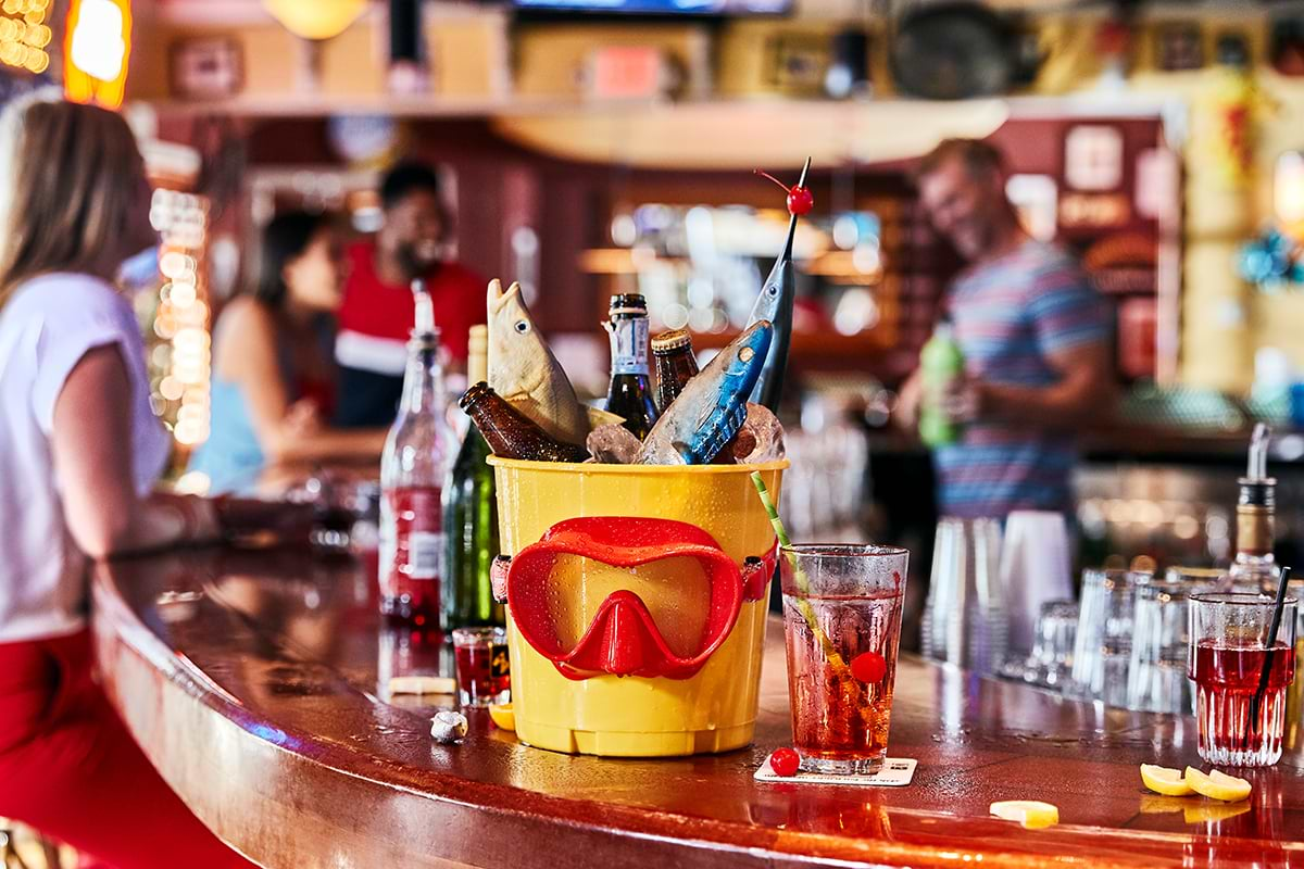 Yellow bucket with beers and fish at bar's bar. People on the background chatting 