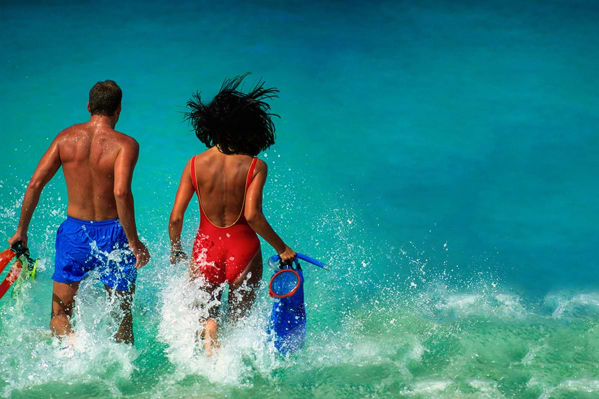 A man and woman run into the ocean with snorkeling gear.