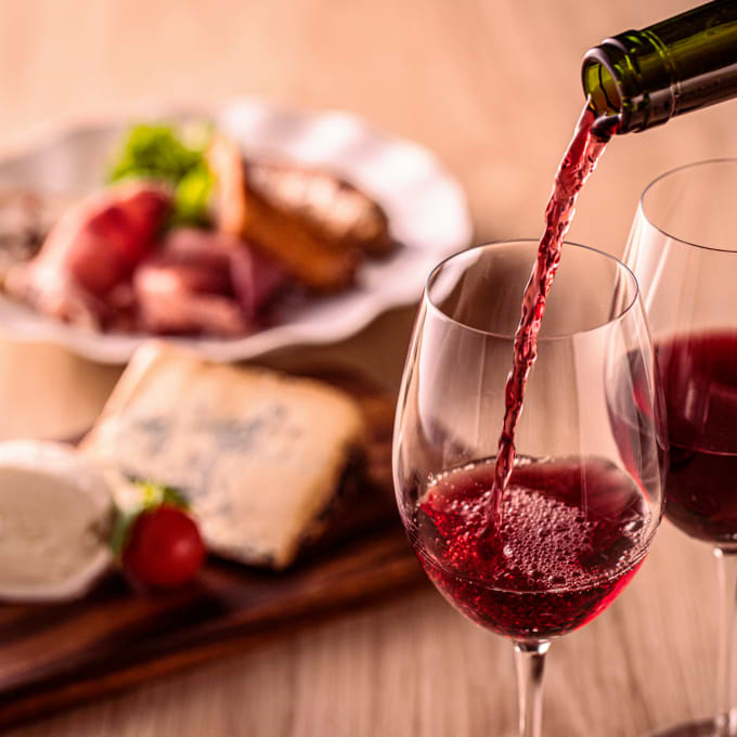 Red wine being poured from a bottle into a glass, with food in the background.