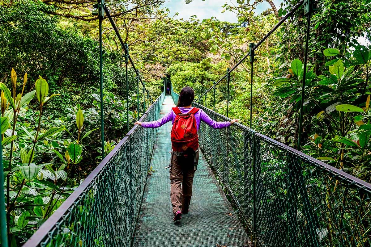Woman on a hanging bridge over a lush jungle.